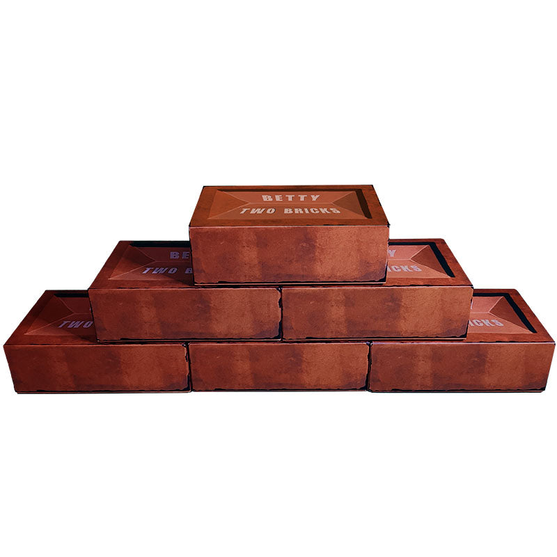 A stack of 6 Betty Two Bricks game boxes which are shaped and designed to look like bricks stacked in a pyramid with 3 on the bottom, 2 in the middle and one on top.