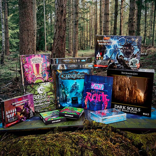 Image of a pile of board games and tabletop accessories in a forest with tall trees.