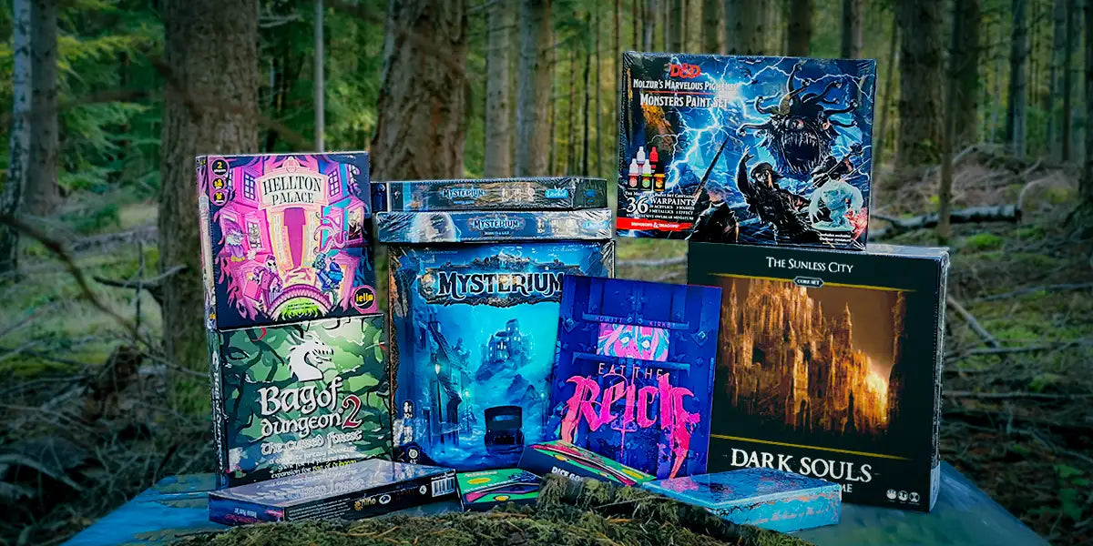 Image of a selection of board games piled up together in the woods for Halloween/Samhain. The games pile includes Hellton Palace, Bag of Dungeon 2, Mysterium and its two expansions, Eat the Reich, Dark Souls, Betrayal and the D&D Molzur's Marvellous Pigment: Monster's Paint Set along with Dice Goblin's The Deathknight and The Fiendish sets.