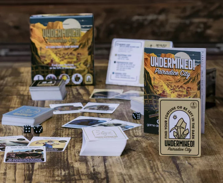 Image of Undermined! Pairadice City game cards and rule leaflet on a table. This game by Devilfly Games is available at indie online board games and tabletop games retailer Kaioss Games